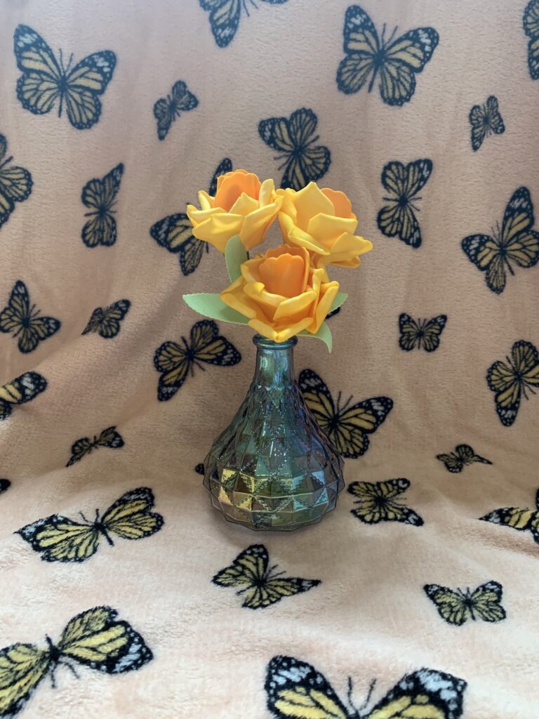 Three yellow roses in a bud vase surrounded by butterflies